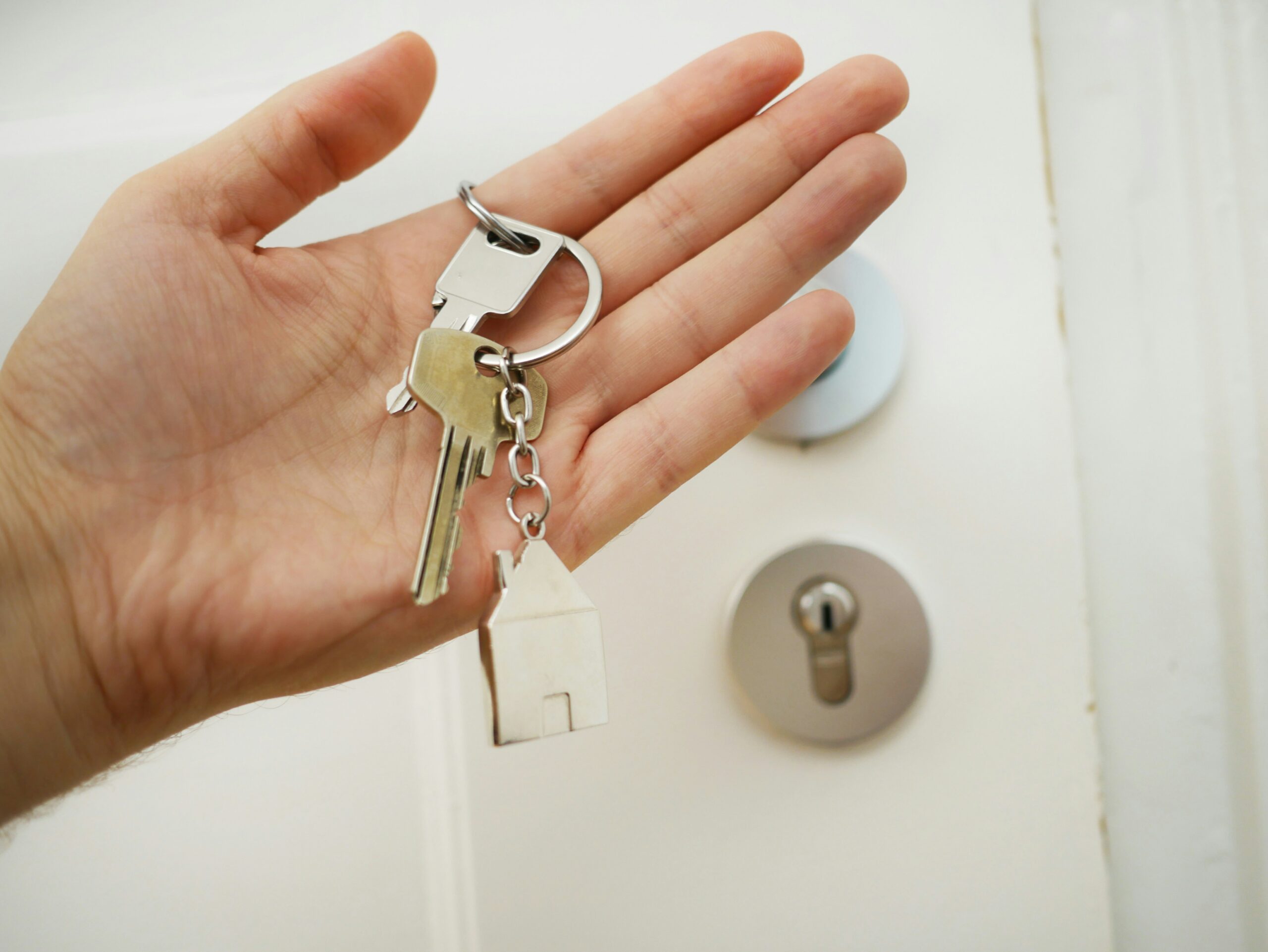 Hand met een sleutelbos en een huisvormige sleutelhanger voor een voordeur