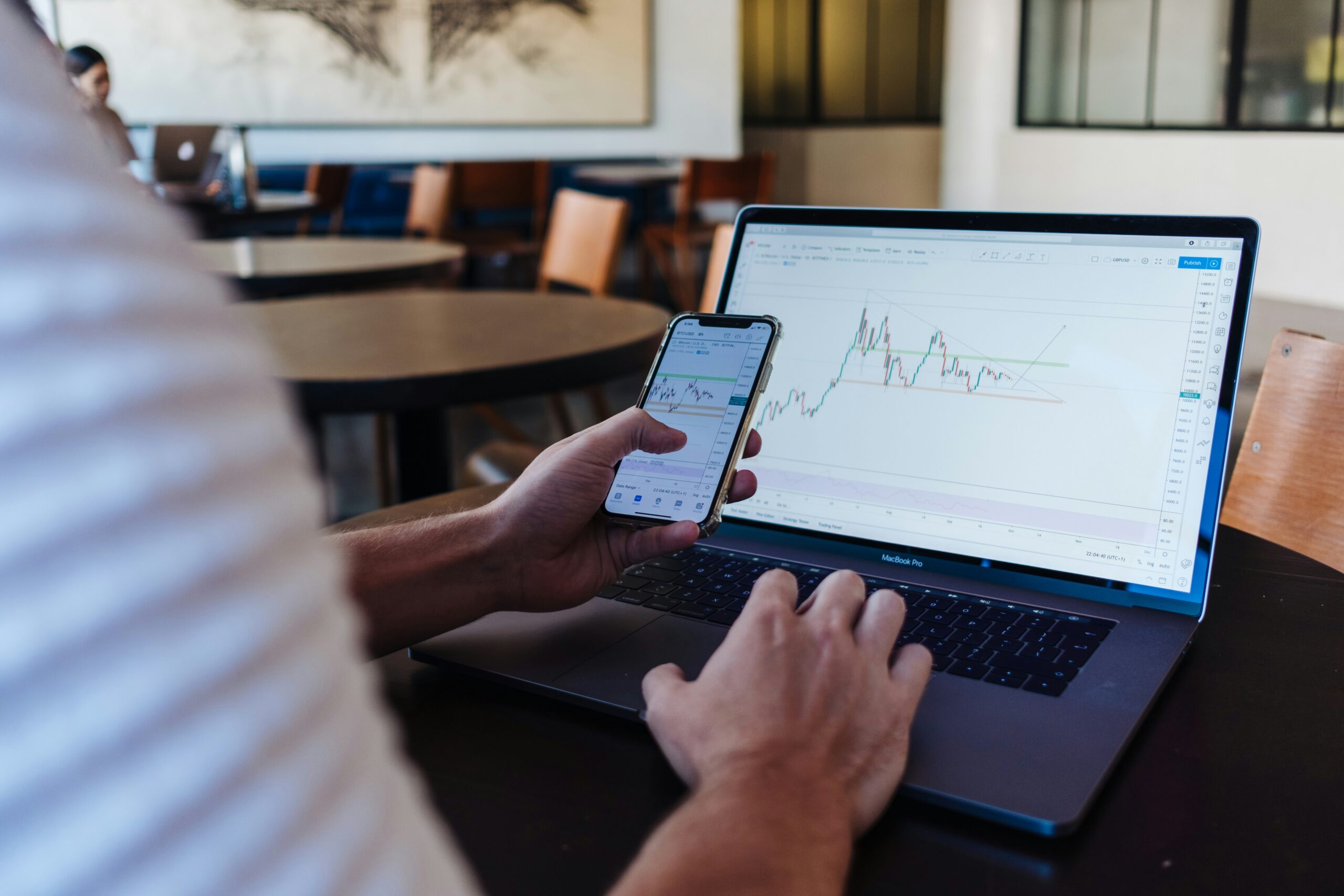 Persoon aan een laptop met een beleggingsplatform en een smartphone met beurskoersen